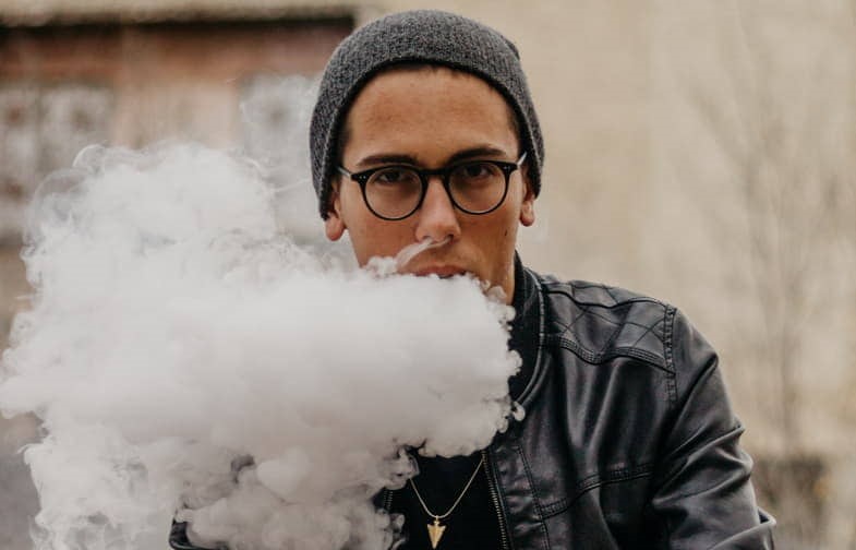 Boy with glasses vaping and emitting a big cloud of vapour